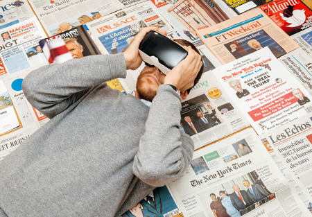PARIS, FRANCE - JAN 21, 2017: Man wearing VR Virtul Reality map above major international newspaper journalism featuring headlines with Donald Trump inauguration as the 45th President of the United States in Washington, D.Cのeditorial素材