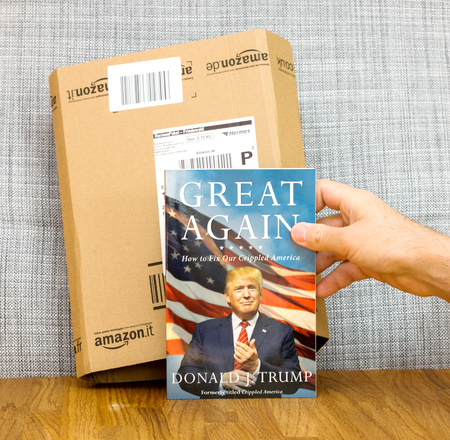 PARIS, FRANCE - FEB 9, 2017: Man holding book Great Again - how to fix our crippled America biography book by Donald J Trump in front of Amazon delivery box. Crippled America: How to Make America Great Again is a book by Donald Trump, published by Simon &のeditorial素材