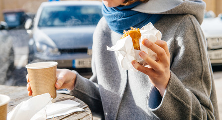 Elegant woman eating traditional Toulouse sausage roll drinking coffee outdoor in the city of Bristol, United Kingdomの写真素材