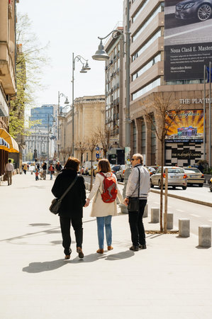 BUCHAREST, ROMANIA - APR 1, 2016: Happy adult daughter spending time with her parents - walking on the streets of Bcuharest - holding both parents by handのeditorial素材