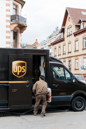 KEHL, GERMANY - APR 6, 2017: Vertical image of UPS United Parcel Service van delivery brown UPS van parked on a street with driver worker searching for the parcel in the van interiorのeditorial素材