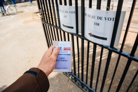 STRASBOURG, FRANCE - APR 23, 2017: French voter registration card held by male hand in front of Bureau de Vote Voting Section open for the 2017 French presidential elections posted outside a polling station blak and whiteのeditorial素材