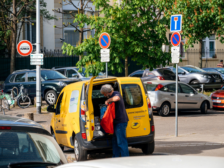 STRASBOURG, FRANCE - APR 12, 2017: Yellow van of La Poste - French National Postal service with postal driver worker searching gor the right parcel to deliver near French buildingのeditorial素材