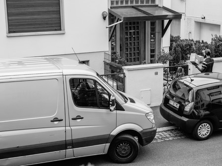 PARIS, FRANCE - JUL 12, 2017: Black and white  Aerial view of delivery man with cardboard parcel box writing info notice to absent client to come back later to the the consignee to deliver the cardboard parcelのeditorial素材