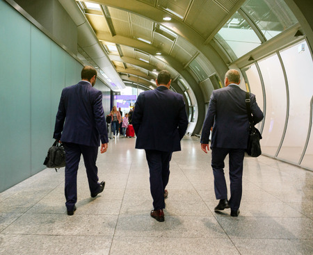 Rear view of three executive businessmen walking toward the end of the international airport terminal to take the plane for the upcoming business meetingの写真素材