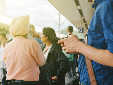 Side view of man holding smartphone in crowded strain station waiting for the fast train on the...