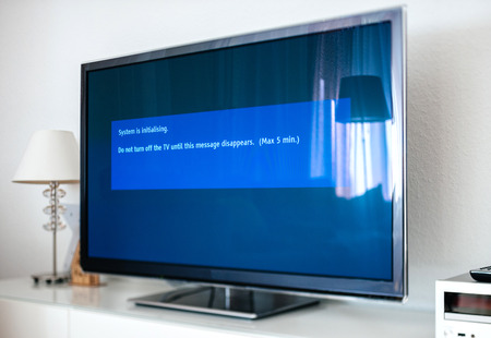 Update install process of system update software process on a modern television set in living room with message System is initializing, do not turn TVの写真素材