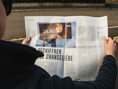 PARIS, FRANCE - SEP 24, 2017: Side view of woman reading latest newspaper Le Monde with article investigation about Angela Merkel before the election in Germany for the Chancellor of Germany, the head of the federal governmentのeditorial素材