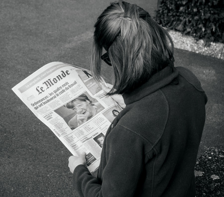 PARIS, FRANCE - SEP 24, 2017: View from above of woman reading latest newspaper Le Monde with portrait of Angela Merkel before the election in Germany for the Chancellor of Germany, the head of the federal governmentのeditorial素材
