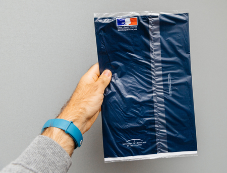 PARIS, FRANCE - OCT 4, 2017: Man holding against gray background envelope containing Taxe d'habitation (rates, property tax) which is sent once per year to very household owner or people who rent a house apartmentのeditorial素材