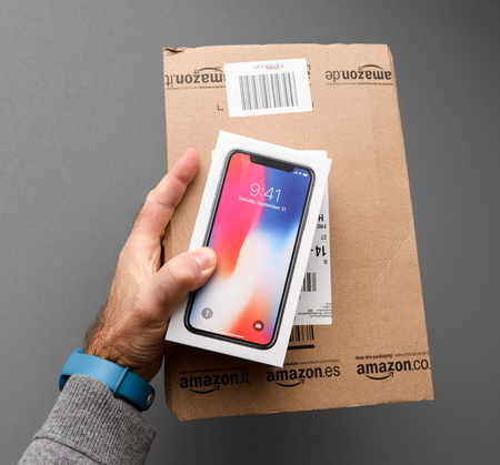 PARIS, FRANCE - NOV 3, 2017: Man holding against gray background the colorful box of the latest Apple iPhone X 10 smartphone and Amazon Prime boxのeditorial素材