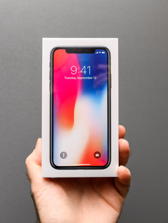 PARIS, FRANCE - NOV 3, 2017: Man holding against gray background the colorful box of the latest most wanted Apple iPhone X 10 smartphoneのeditorial素材