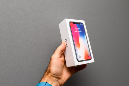 PARIS, FRANCE - NOV 3, 2017: Man holding against gray background the colorful box of the latest Apple iPhone X 10 smartphoneのeditorial素材
