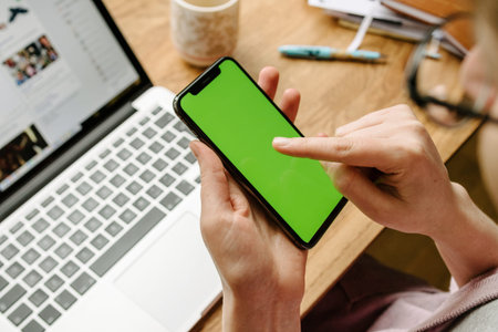 PARIS, FRANCE - NOV 5, 2017: POV of woman testing the new Apple iPhone X 10 smartphone (with Chroma Key Backgrounds) in creative room environment table  with Facebook Social network running on the Apple MacBook Pro laptopのeditorial素材