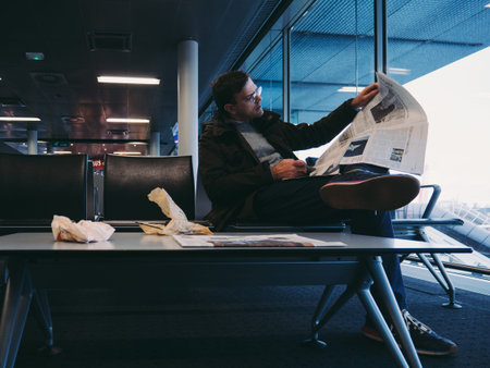 BASEL, SWITZERLAND - NOV 11, 2017: Businessman in casual clothes reading the New Yourk Times newspaper in the waiting lounge hall chair in EuroAirport Basel Mulhouse Freiburgのeditorial素材