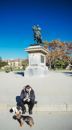 BARCELONA, SPAIN - NOV 12, 2017: Spanish man with two small dogs using smartphone near Estatua equestre del general Prim statue monument in Parc de la Ciutadella on a warm summer sunny dayのeditorial素材