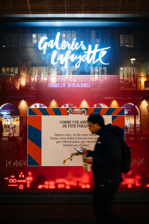 STRASBOURG, FRANCE - NOV 21, 2017: Man checking phone and eating while passing by Galeries Lafayette shop display in preparation for Christmas decorationのeditorial素材