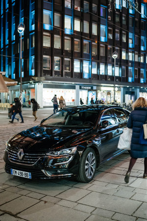 STRASBOURG, FRANCE - NOV 21, 2017: Shopper passing by luxury black Renault Talisman reflecting red Christmas light decorations at nightのeditorial素材