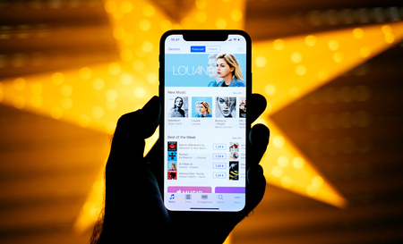 PARIS, FRANCE - NOV 10, 2017: Man holding the new Apple iPhone X 10 Display with yellow star bokeh background featuring Best of The week iTunes Louane chartsのeditorial素材