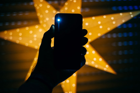 Man holding the new Phone with yellow star bokeh background featuring a blick light from the rear flash and camera - holiday concept の写真素材