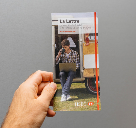 PARIS, FRANCE - NOV 28, 2017: Man hand holding against gray background the official HSBC bank newsletter La Lettre for French bank clientsのeditorial素材