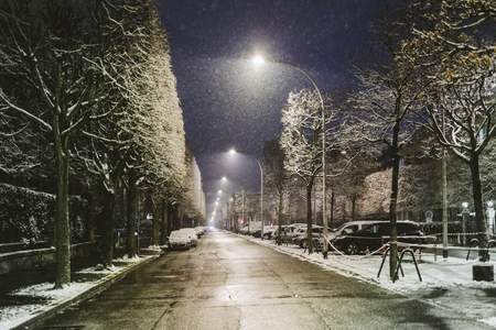 Snowing in French city at night with empty street and covered with snow carsの写真素材