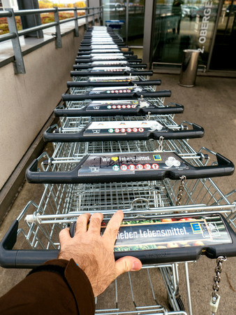 FRANKFURT, GERMANY - NOV 4, 2017: Man hand POV over the WANZL supermarket cart in front of the entrance with Eingang sign to the Edeka store - paying for the rent of the cartのeditorial素材