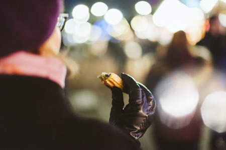Rear view of French woman wearing fashionable beret hat eating traditional Christmas waffle food from the food truck with defocused Christmas market in the backgroundの写真素材