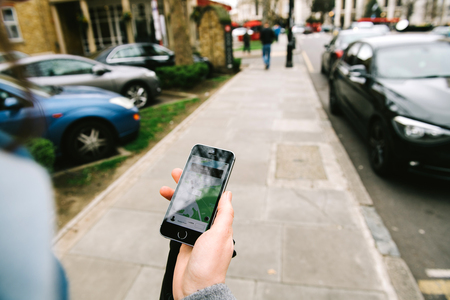 GREENWICH, LONDON, UNITED KINGDOM - MAR 10 2017: Woman order waiting for the UBER taxi cab on British street  - point of view looking at the phone on the streetのeditorial素材