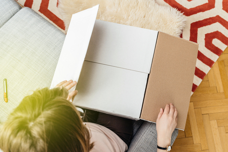 View from above of woman unboxing unpacking white cardboard box containing online shopping bought goodの写真素材