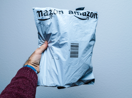 PARIS, FRANCE - JAN 23, 2018: Man holding against white background a plastic parcel delivery of Amazon package containing clothes or shoesのeditorial素材