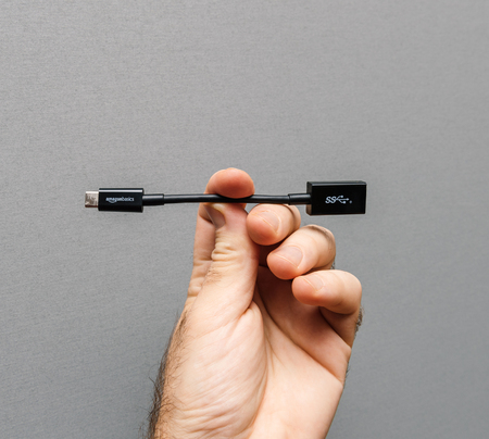PARIS, FRANCE - JAN 23, 2018: Man holding against gray background a new black cable from Amazon Basics AmazonBasics with USB-C to USB  Adapterのeditorial素材