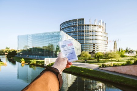 STRASBOURG, FRANCE - APR 23, 2017: Man holding French voter registration card Carte Electorale with the European Parliament politics building in the backgroundのeditorial素材