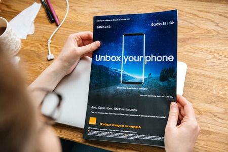 PARIS, FRANCE - APR 26, 2017: Woman reading Unbox Your Phone advertising campaign for Samsung Galaxy Smartphone S8 in French from Orange Telecom in magazine newspaperのeditorial素材