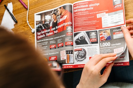 PARIS, FRANCE - APR 26, 2017: Elevated view woman reading A.T.U Auto-Teile-Unger German automotive services advertising leaflet with accessories and car care products such as warrantyのeditorial素材