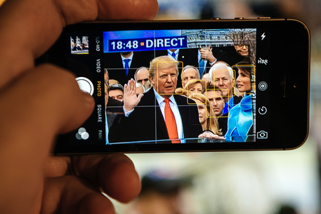 PARIS, FRANCE - JAN 20, 2017: Man watching TV news reporting 45th U.S. President Donald Trumps inauguration ceremony - taking oath of officeのeditorial素材