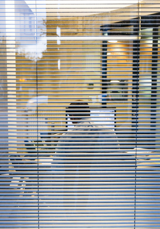 Silhouette of working late businessman man seen through windows blinds working report thesis data analysis bank report view from the street - working late concept businessの写真素材