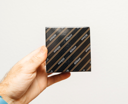 PARIS, FRANCE - JAN 23, 2018: Man holding against gray background a box of Nikon accessory for camera microscope or optic equipmentのeditorial素材