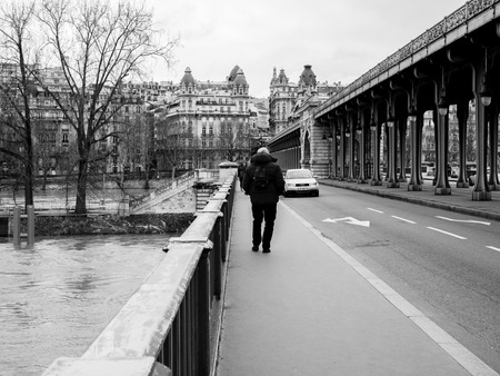 PARIS, FRANCE - JAN 30, 2018: Rear view of senior man walking on the Pont de Bir-Hakeim bridge watch the swollen river Seine after days of heavy rainのeditorial素材