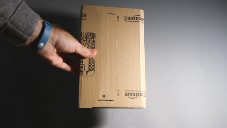 PARIS, FRANCE - FEB 7, 2018: Man showing Amazon prime cardboard box - unboxing the book, electronic gadget, gift against gray backgroundのeditorial素材