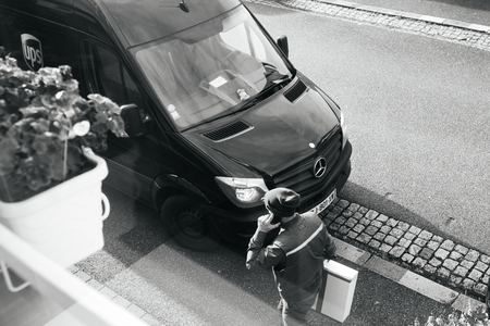 PARIS, FRANCE - FEB 16, 2018: Courier enters UPS United PArcel Service brown delivery van with cardboard parcel in the hands delivering the on time delivering package parcel - view from above black adn whiteのeditorial素材