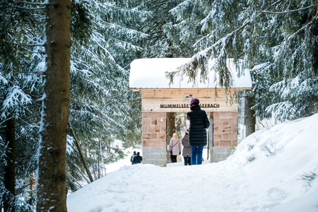 MUMMELSEE, GERMANY - FEB 18, 2018: Winter day with snow and tower gate Mummelseetor Seebach and woman walking underneath on discovering the mountains in Germanyのeditorial素材