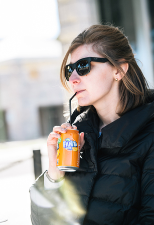 LISBON, PORTUGAL - FEB 10, 2018 Beautiful American woman drinking Fanta Soda juice can through straw at the sunny terrace in Lisbon centerのeditorial素材