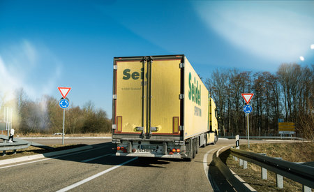 BADEN WURTTEMBERG, GERMANY - FEB 25, 2018: Driver point of view POV at the driving in front large yellow haulage truck transporting industrial goods - entering roundaboutのeditorial素材