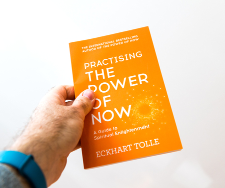 PARIS, FRANCE - FEB 21, 2018: Man holding against white background the book of Eckhart Tolle Practising the power of nowのeditorial素材
