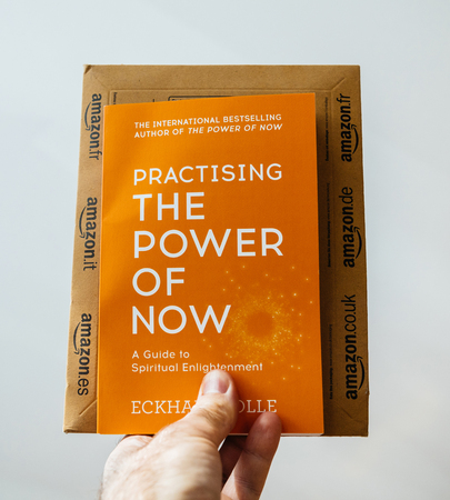 PARIS, FRANCE - FEB 21, 2018: Man holding against white background the book of Eckhart Tolle Practising the power of now and Amazon.com envelopeのeditorial素材