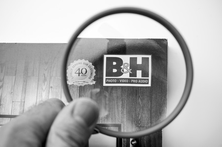 PARIS, FRANCE - 14 JAN 2018: B H photo Video pro Audio Magazine catalogue being read by man interested in electronics and technology pov using magnifying glass loupeのeditorial素材