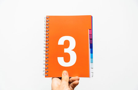 Male hand holding notebook with big number 3 printed on orange color ready for presentation or...