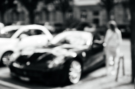 Urban life scene with anonymous woman parking her luxury car on a busy French street - black and...