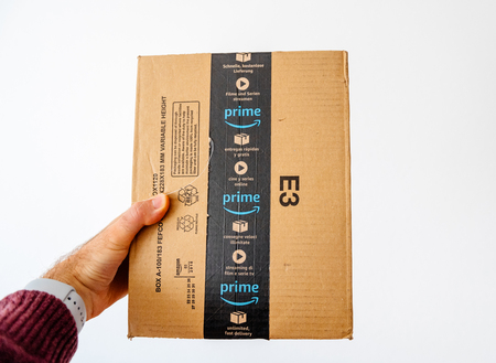 PARIS, FRANCE - APR 20, 2018: Male hand holding the Amazon cardboard box parcel against white isolated backgroundのeditorial素材